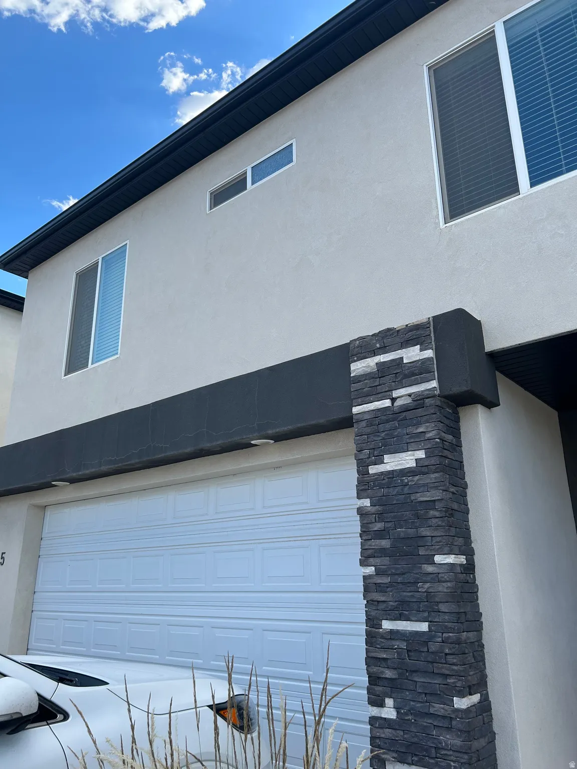 Modern exterior featuring a prominent two-car garage with panel detailing, light stucco siding, and dark stacked stone accents