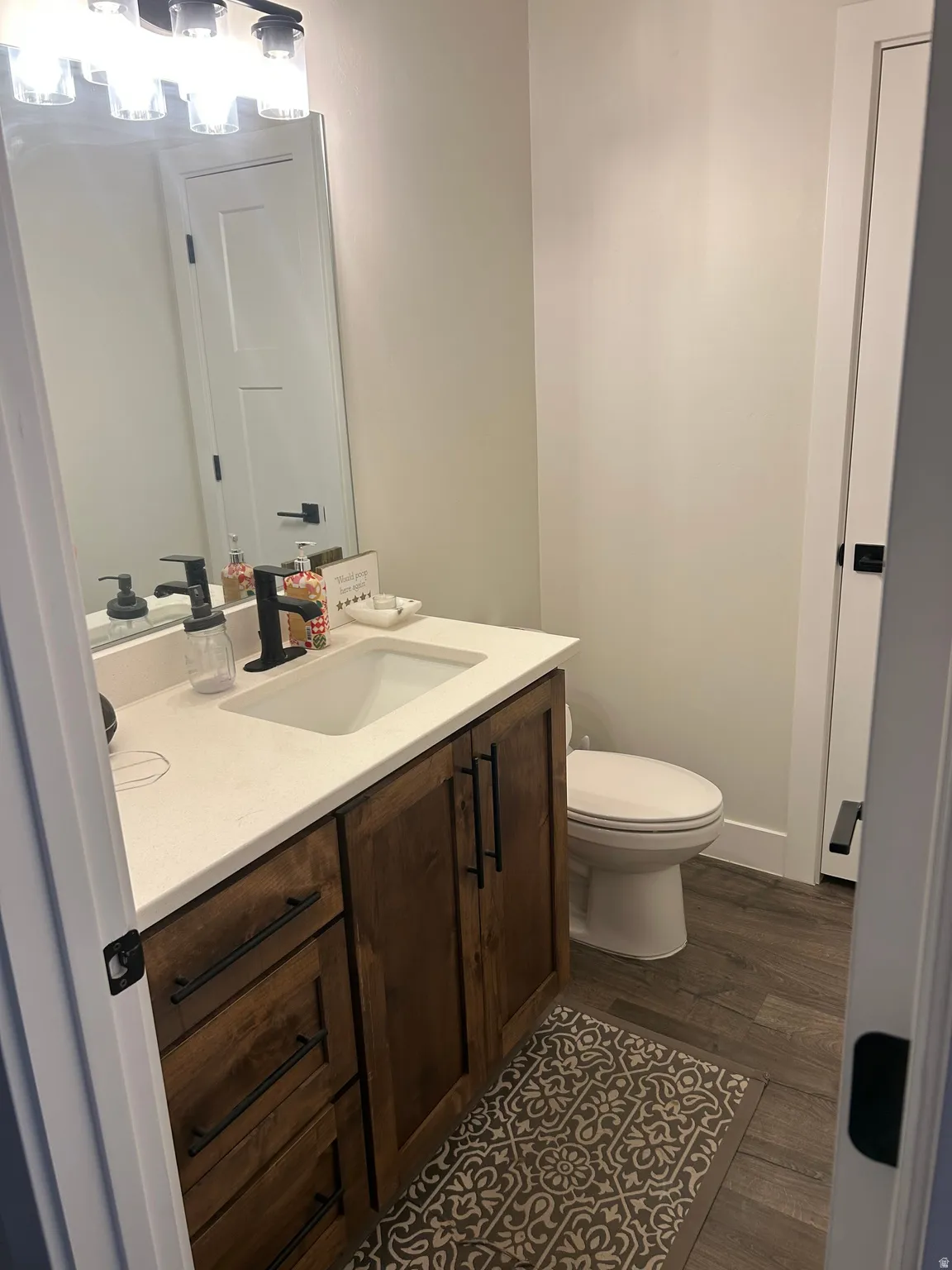 Powder room featuring a wood-finish vanity with drawer and cabinet storage, a white countertop with an integrated sink, a dark-finish faucet, and wood-look floor tiling