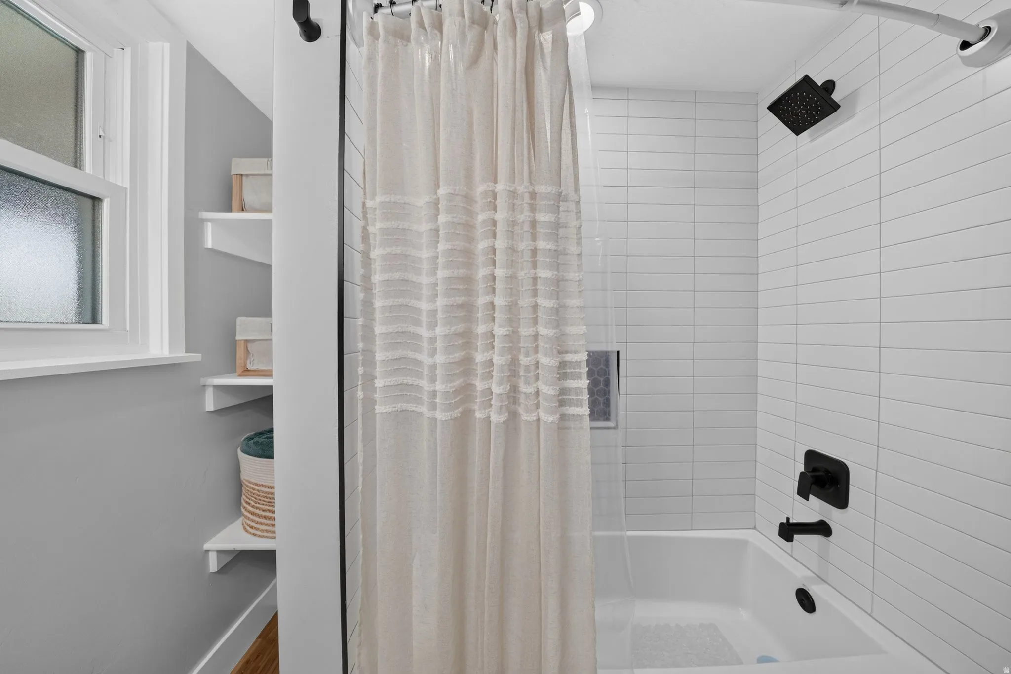 Bathtub-shower combination featuring white subway tile surround, matte black shower fixtures, and a recessed shower niche