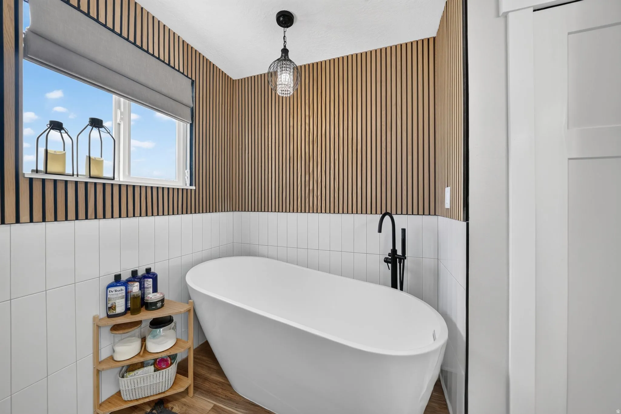 Freestanding soaking tub with a matte black floor-mounted faucet, set against a backdrop of vertical wood slat paneling and white subway tile