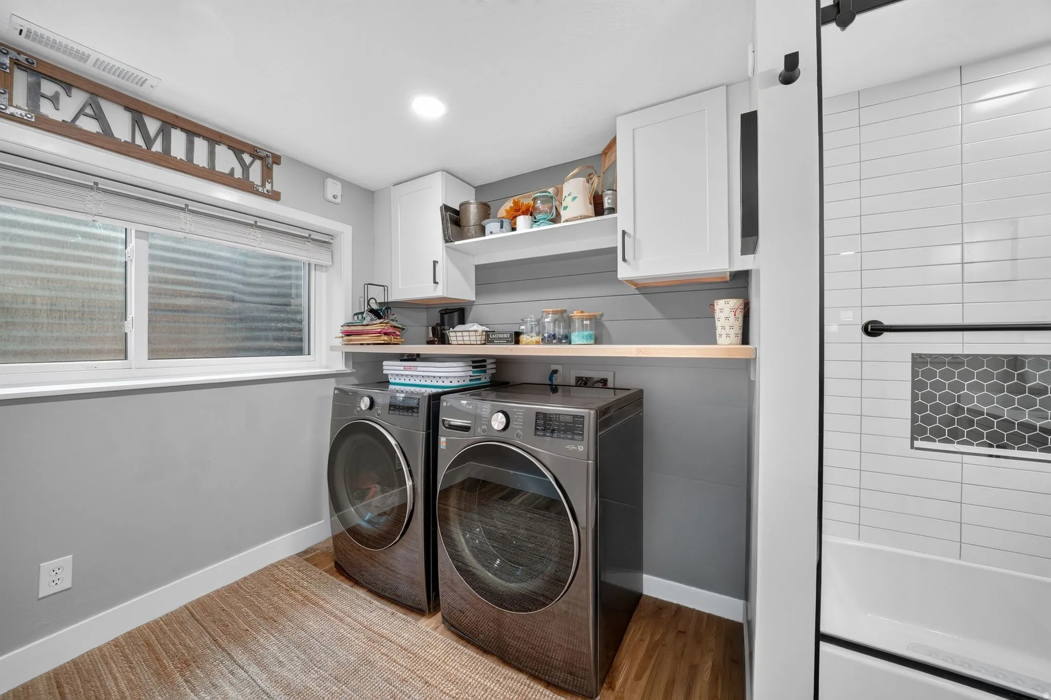 Dedicated laundry area featuring wood-finish flooring, a window providing natural light, white upper cabinetry, and a light wood-tone countertop