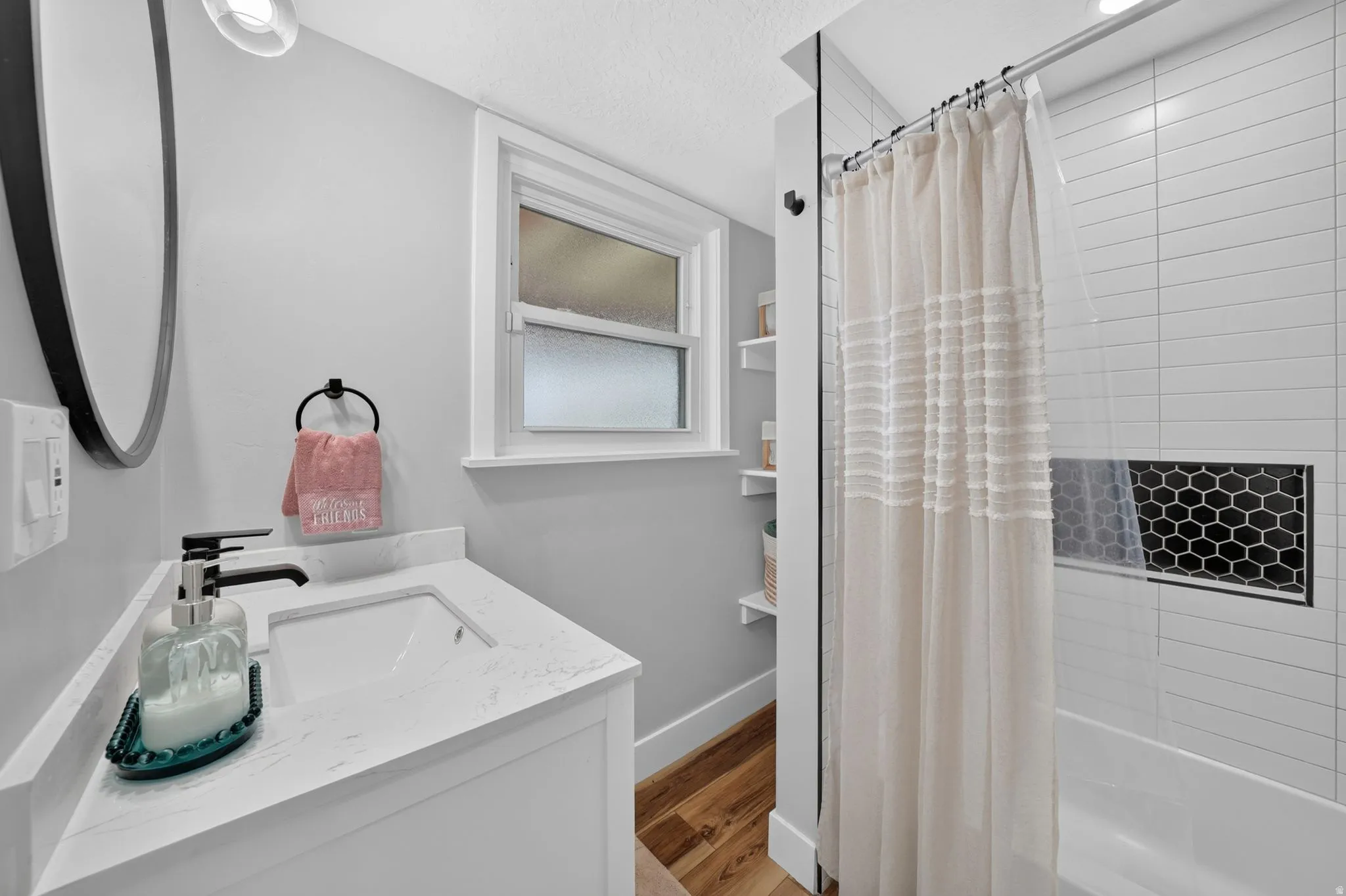 Bathroom featuring a white vanity with an undermount sink and quartz-finish countertop, matte black faucet, and oval mirror