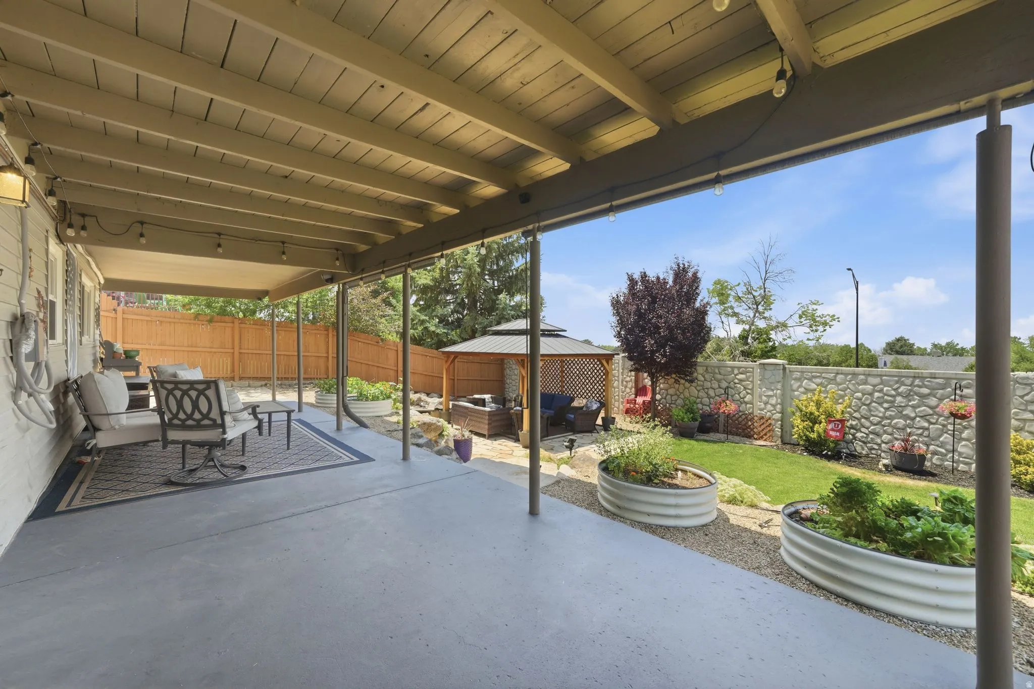 Spacious covered patio area featuring exposed beam ceiling, concrete flooring, and string lighting
