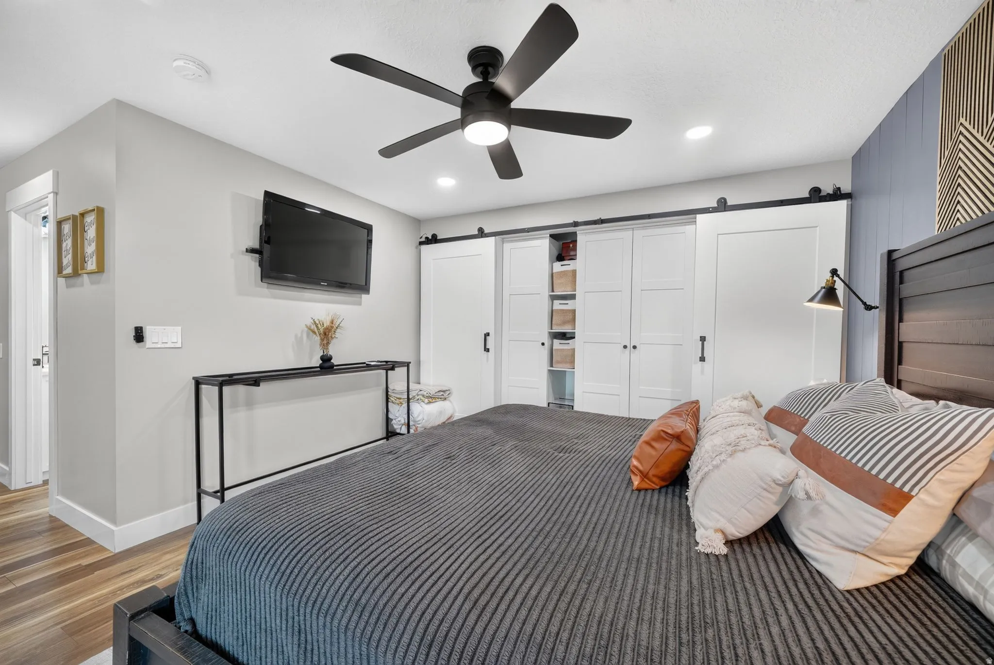 Contemporary bedroom featuring wood-finish flooring and a black ceiling fan with integrated lighting
