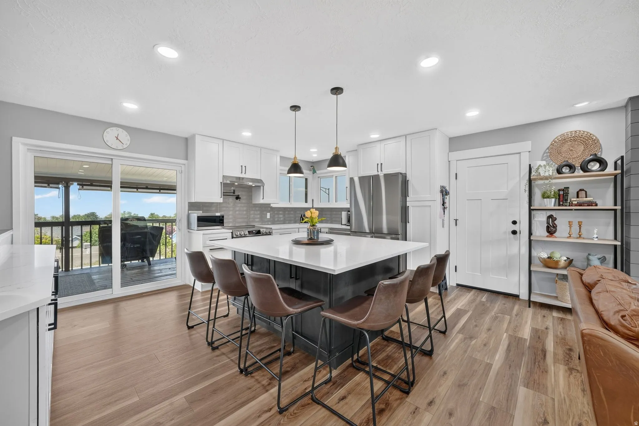 Open-concept kitchen featuring a large central island with seating, white shaker cabinetry, stainless steel appliances, and wood-finish flooring