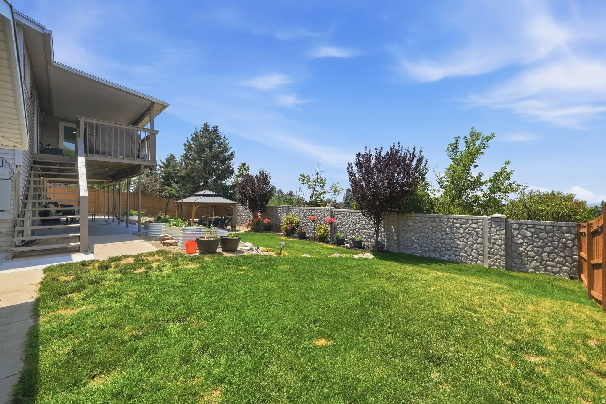 Expansive backyard featuring a stone privacy wall, a covered patio, and a second-story deck with wooden railings