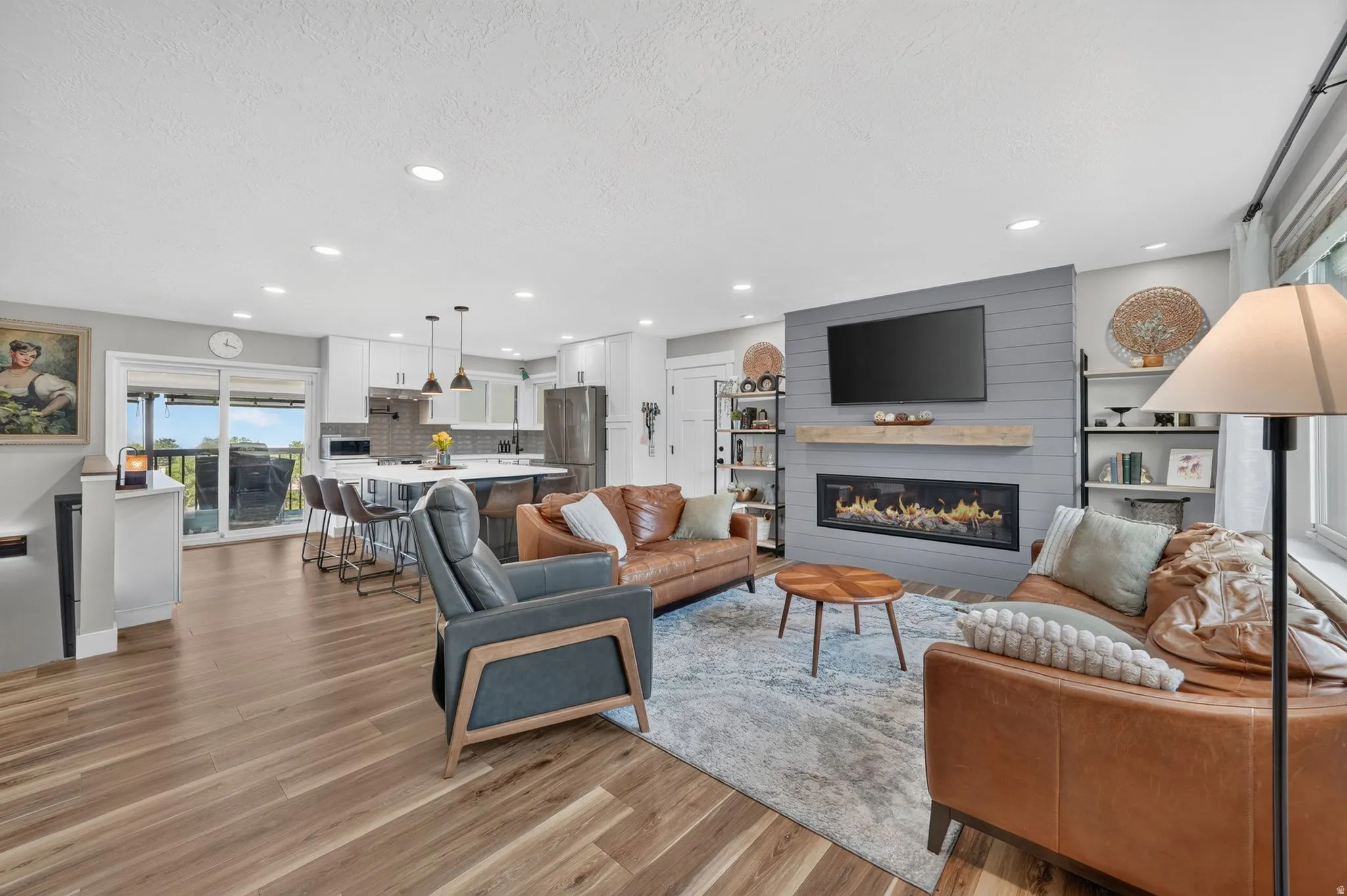 Open-concept living space featuring wood-finish flooring, recessed lighting, and a modern fireplace with a shiplap accent wall
