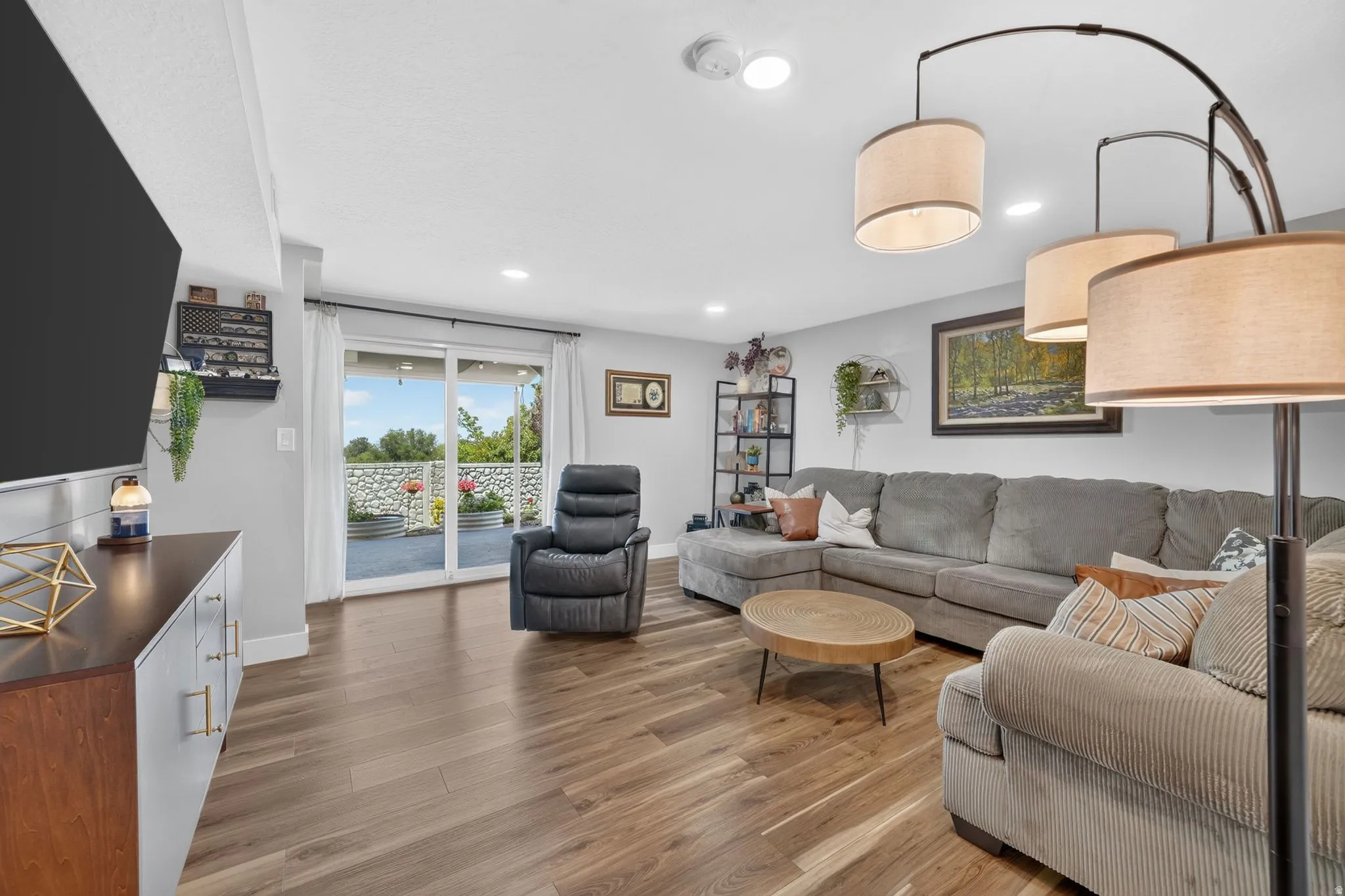 Spacious living area featuring wood-finish flooring, recessed lighting, and a sliding glass door providing natural light and exterior access