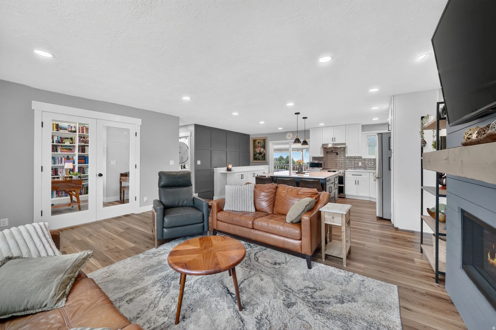 Open-concept living area featuring wood-finish flooring, recessed lighting, and a fireplace with a wood mantel