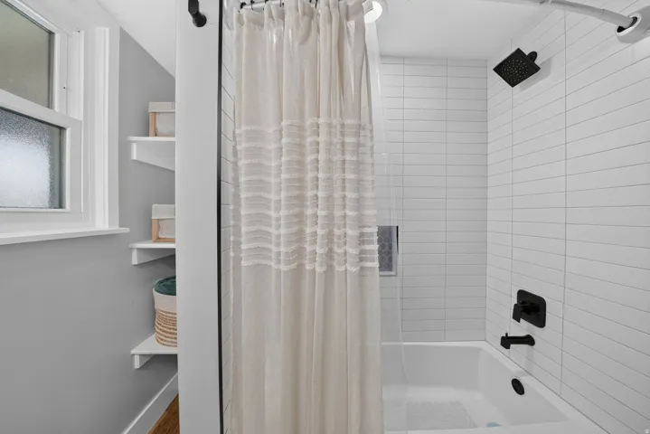 Bathtub-shower combination featuring white subway tile surround, matte black shower fixtures, and a recessed shower niche