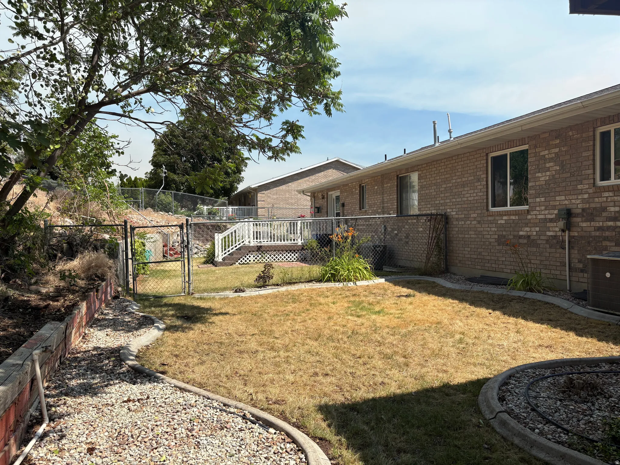 Expansive backyard featuring a partially fenced perimeter, a raised wooden deck with white railing, and decorative gravel pathways