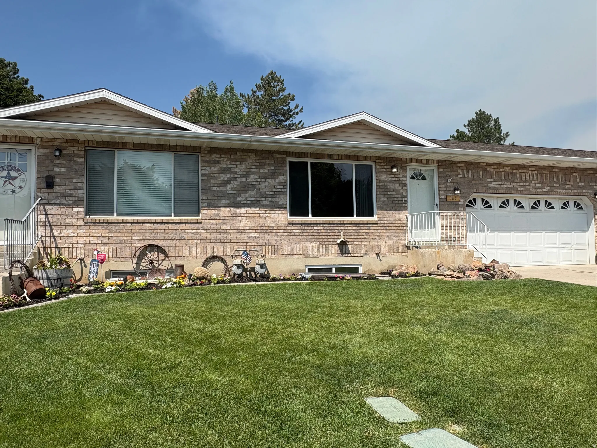 Brick exterior featuring a two-car garage with arched windows, a manicured lawn, and foundational landscaping with decorative elements