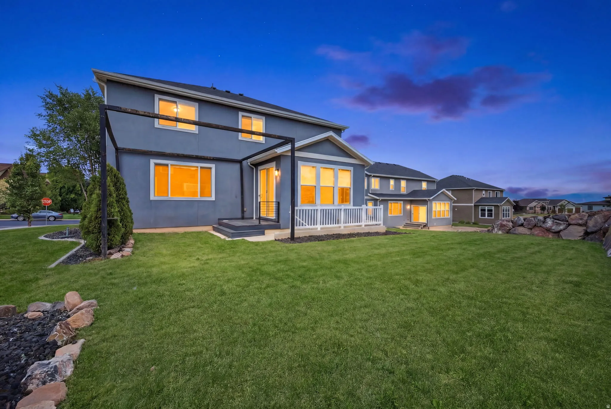 Expansive grassy backyard featuring a white railing deck, a black metal pergola frame, and a decorative rock border