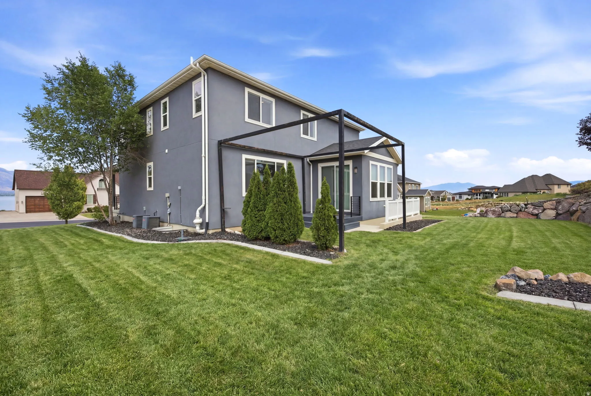 Expansive backyard featuring a manicured lawn, a large pergola structure, and a rock retaining wall