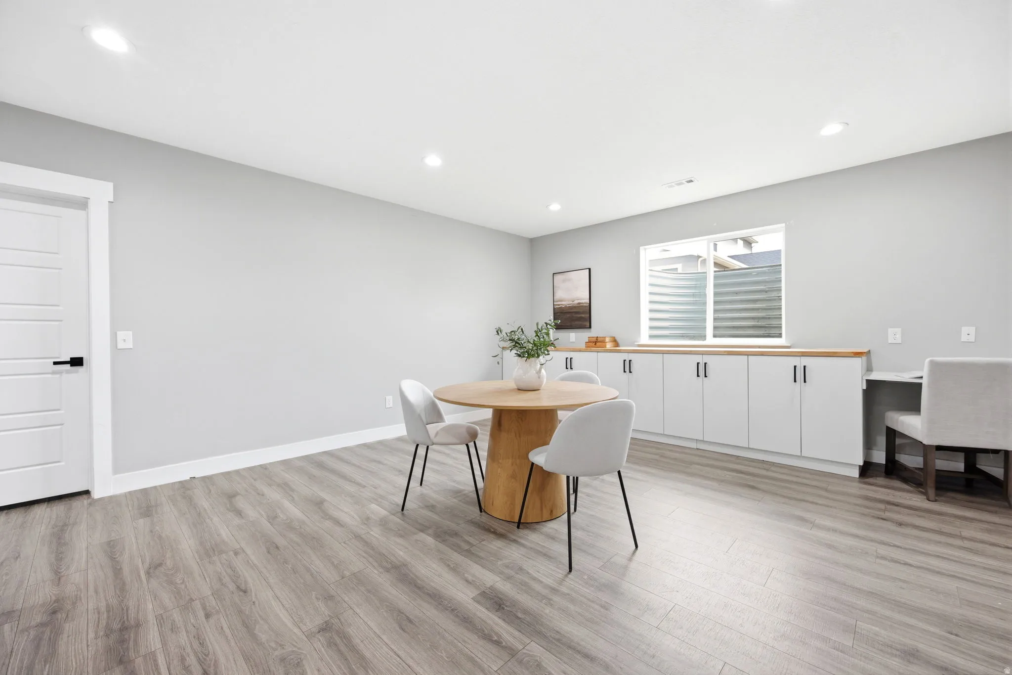 Spacious room featuring light wood-finish flooring, recessed lighting, and a window providing natural light