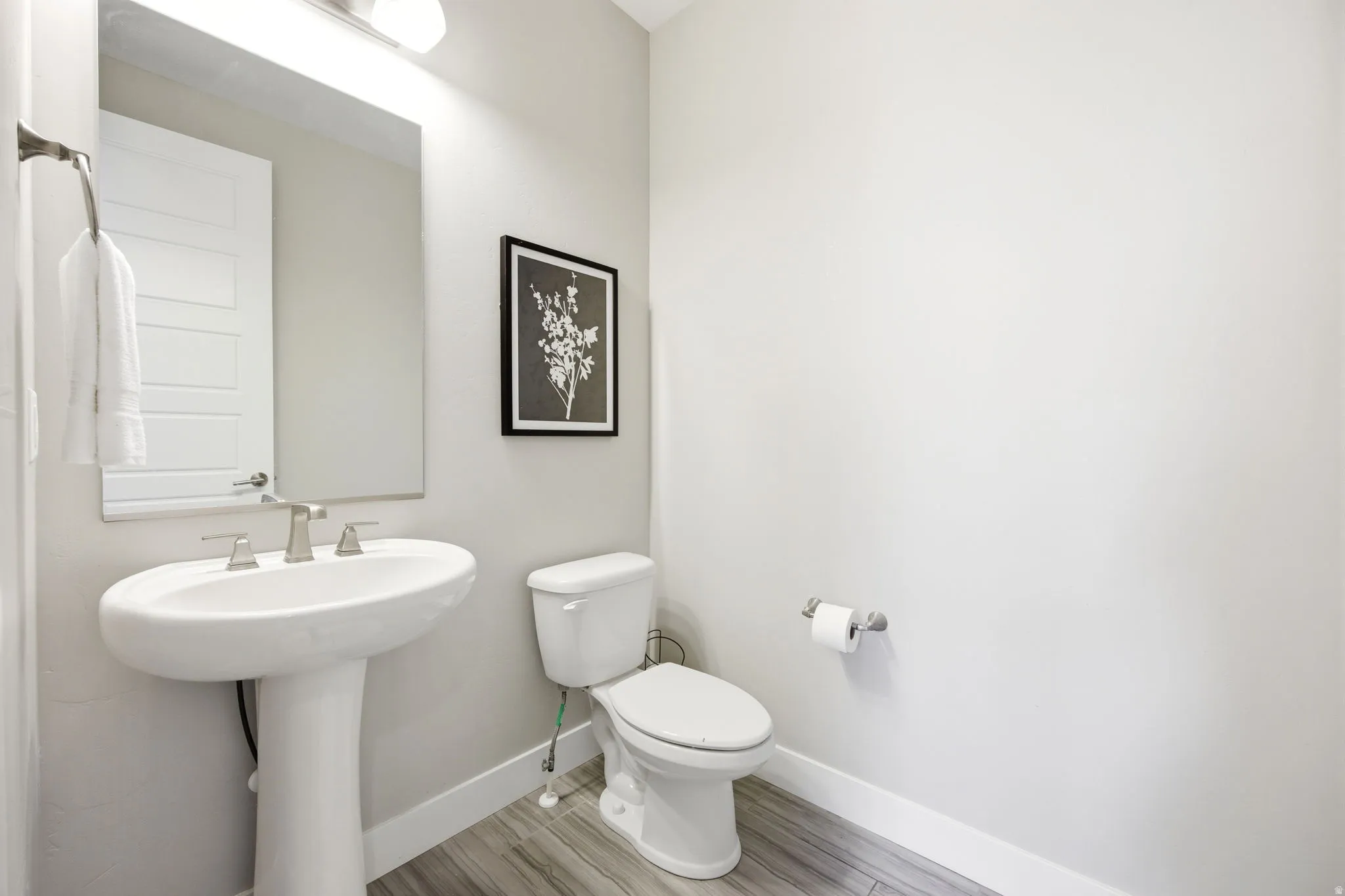 Pedestal sink with a brushed nickel faucet, large wall mirror, and wood-finish flooring