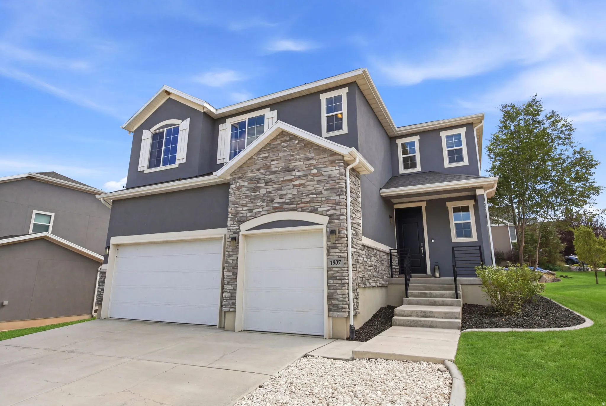 Contemporary stucco exterior featuring stone veneer accents, a two-car garage, and a manicured lawn