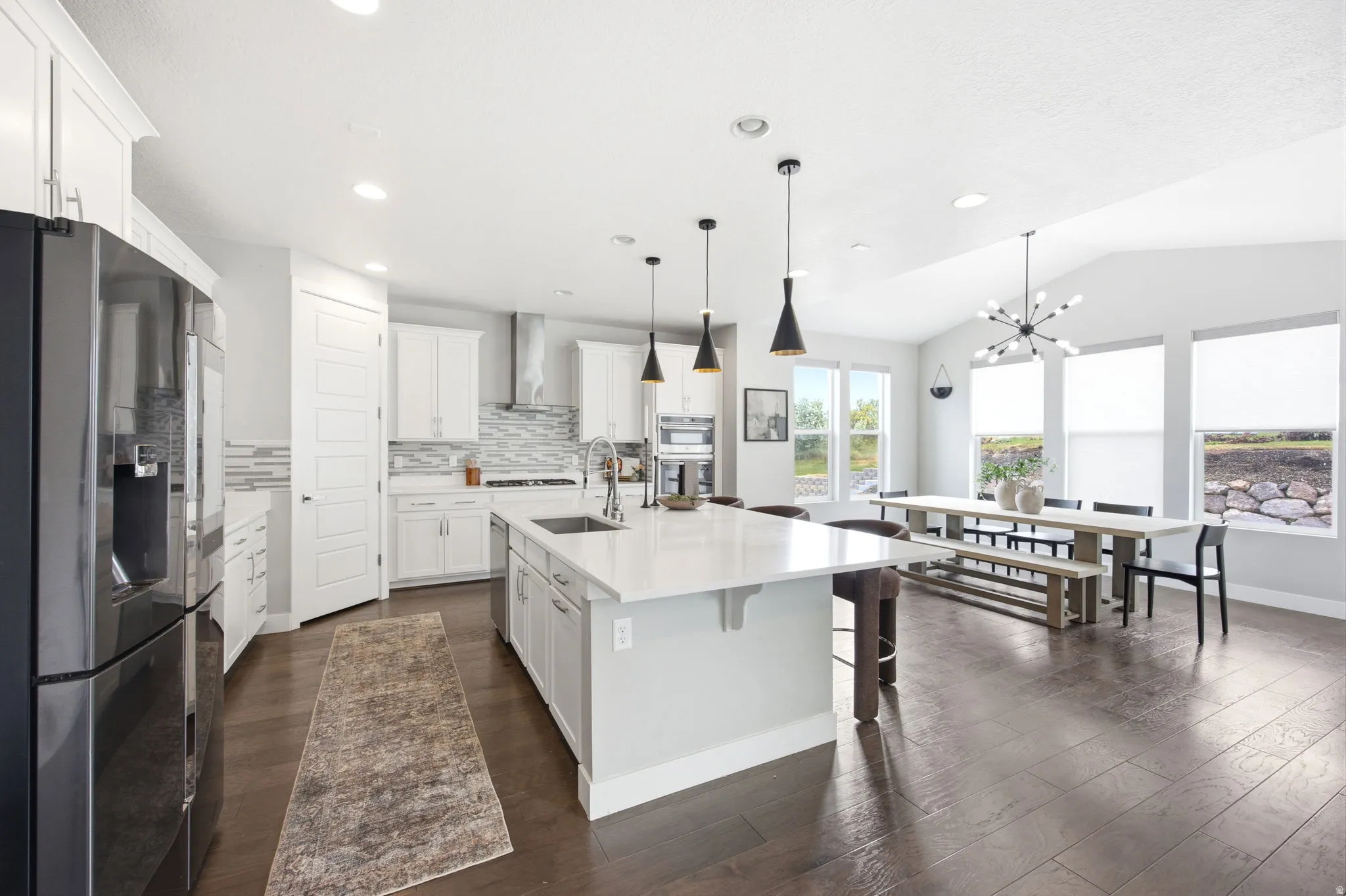 Open-concept kitchen and dining area featuring dark wood-finish flooring, white cabinetry, a large kitchen island with counter seating, and vaulted ceilings with a contemporary chandelier