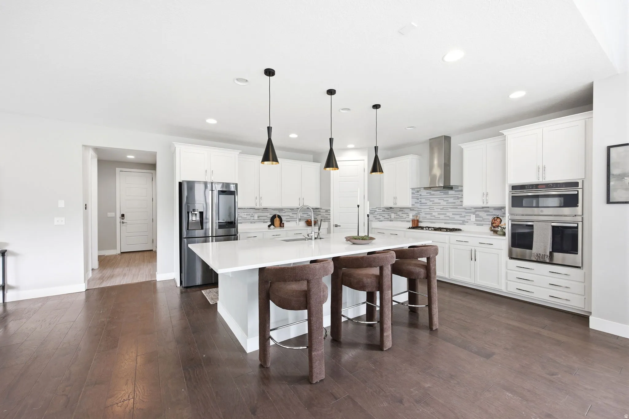 Expansive kitchen featuring a large island with seating, white shaker cabinetry, stainless steel appliances, and wood-finish flooring