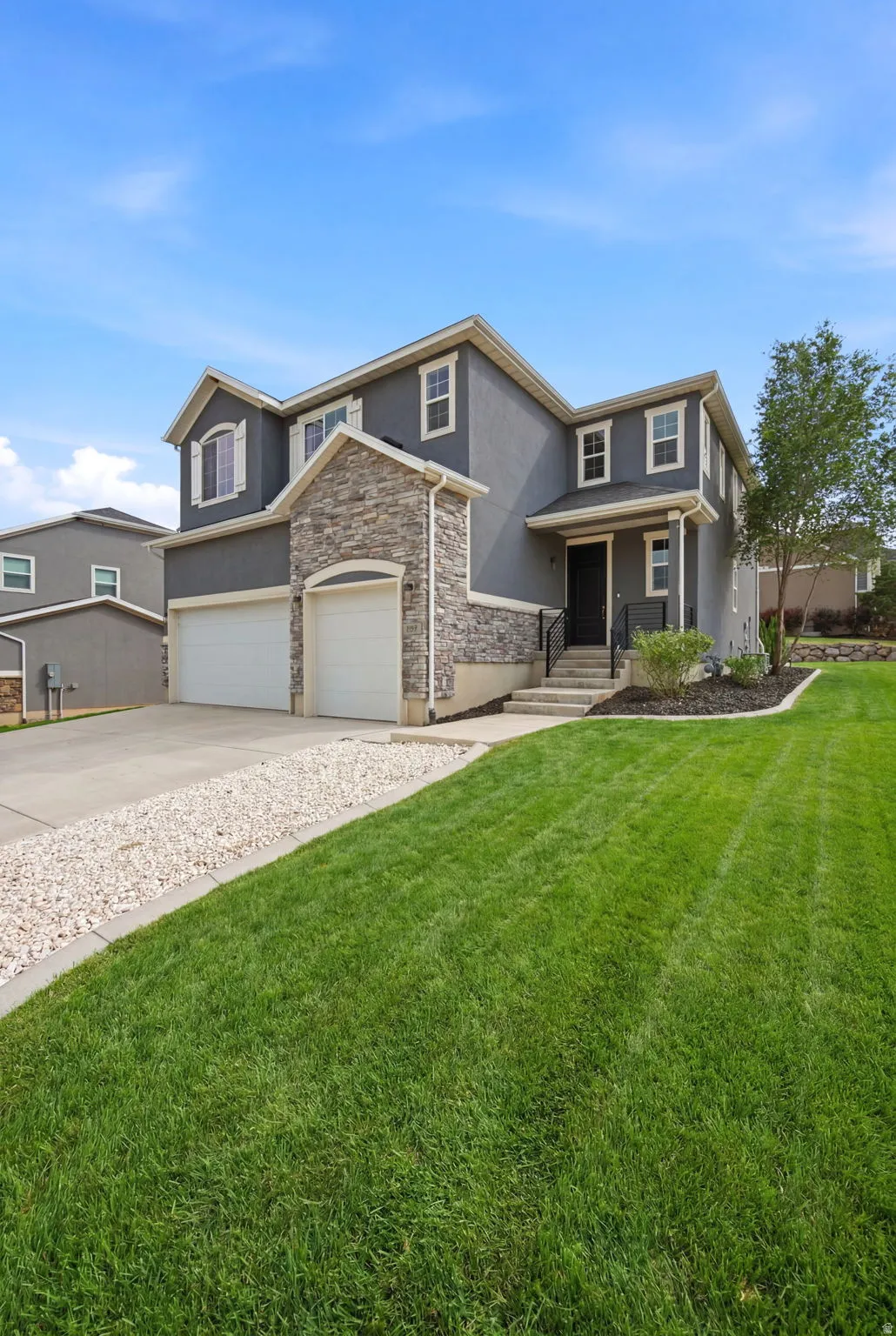 Modern two-story residence featuring a stone and stucco facade, a two-car garage, and a concrete driveway with a gravel border