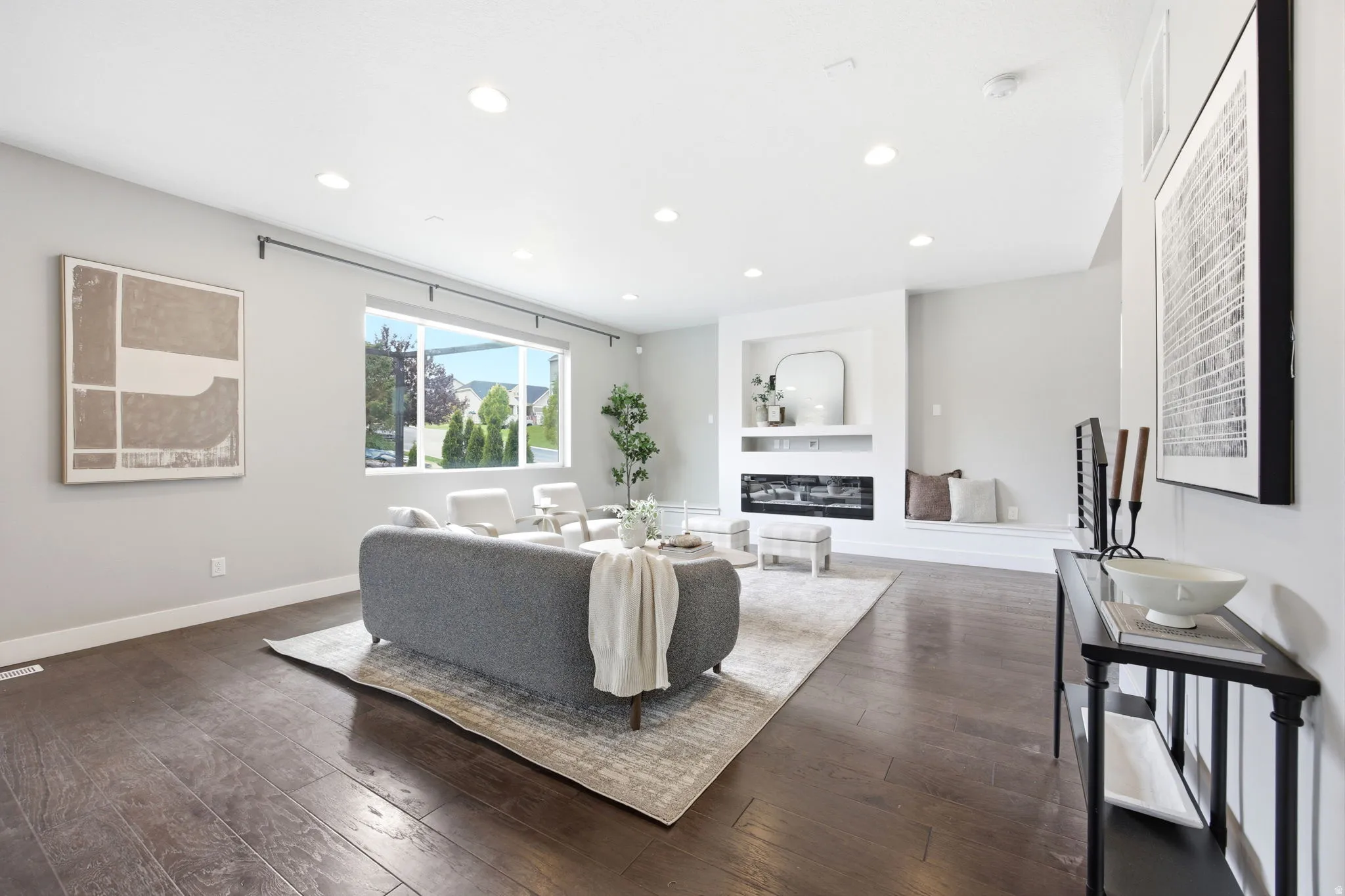 Spacious living area featuring wood-finish flooring, a contemporary fireplace with integrated shelving, recessed lighting, and large windows