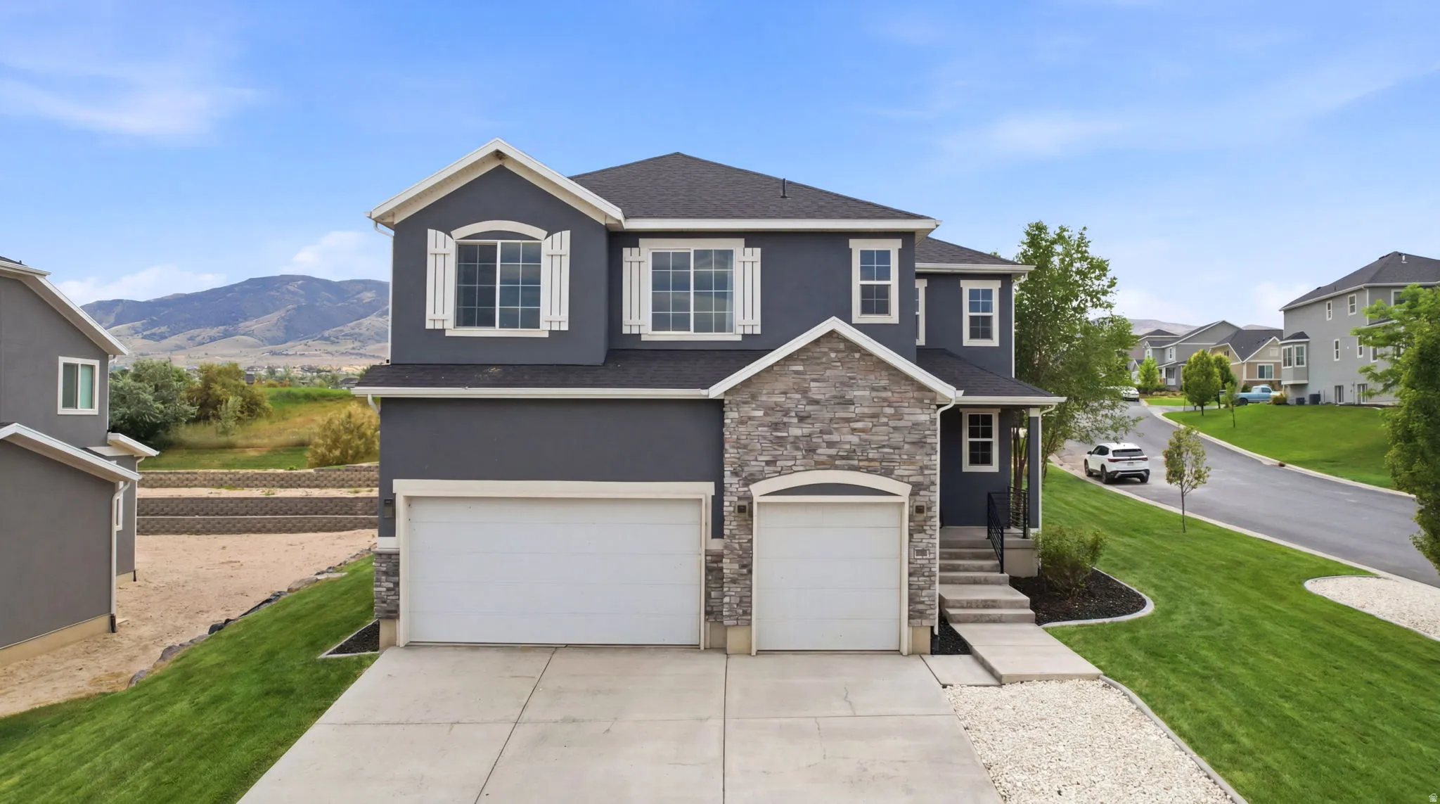 Two-story residence featuring a gray stucco exterior with stone accents and white window shutters