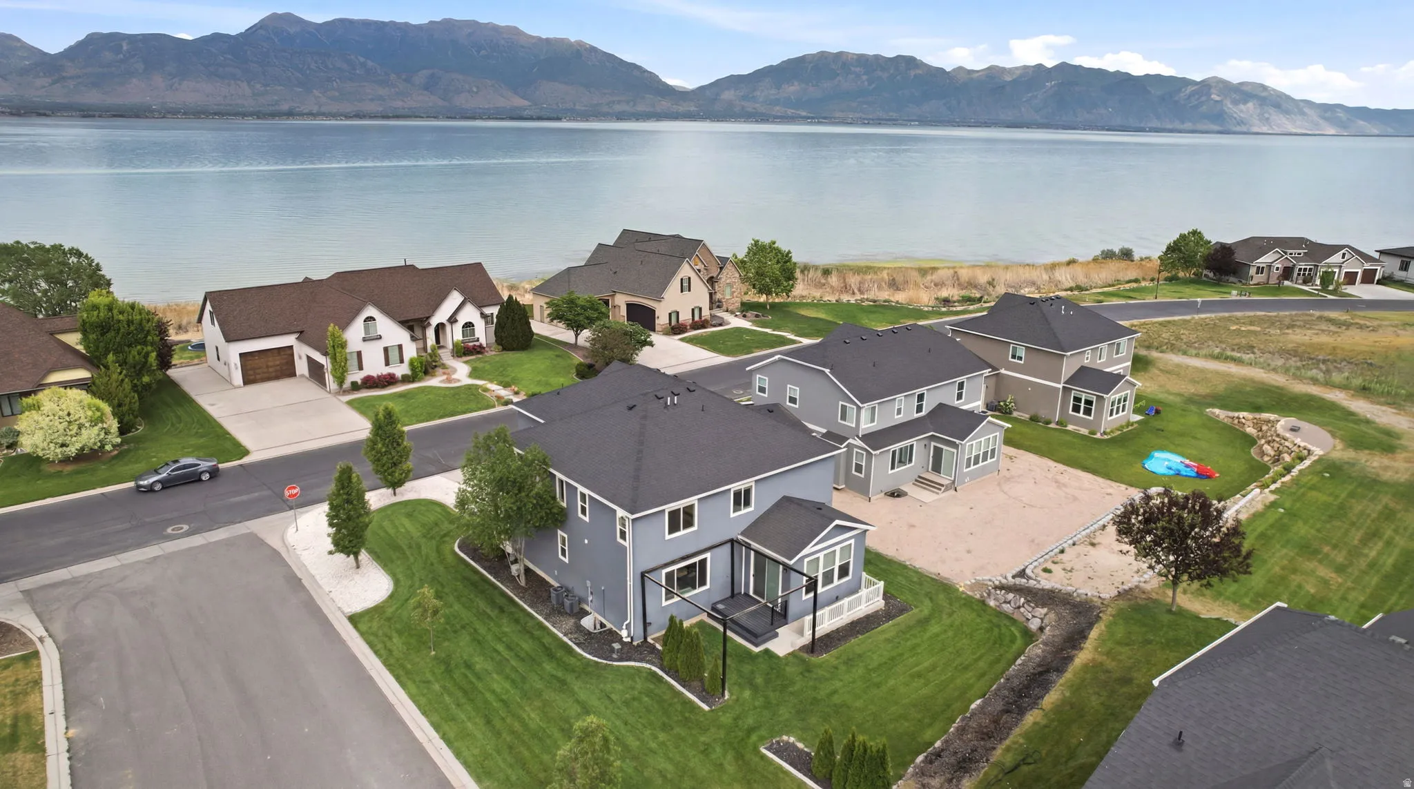 Waterfront community featuring an expansive body of water with distant mountains, paved streets, manicured lawns, and residential structures with dark shingled roofs