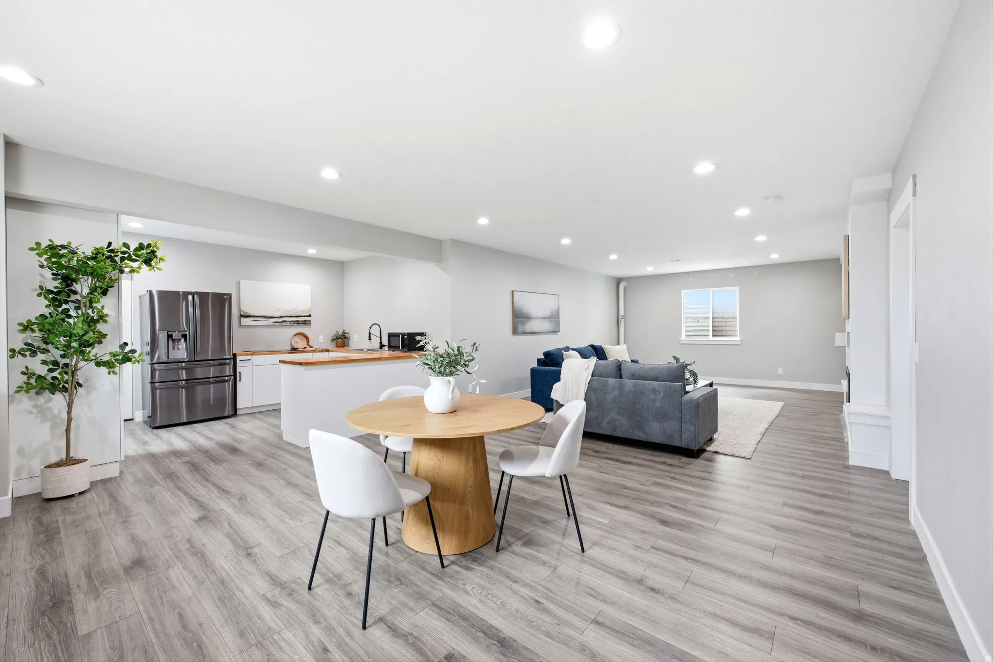Open-concept living area featuring wood-finish flooring, recessed lighting, a modern kitchen with white cabinetry, a kitchen island with a wood countertop, and stainless steel appliances