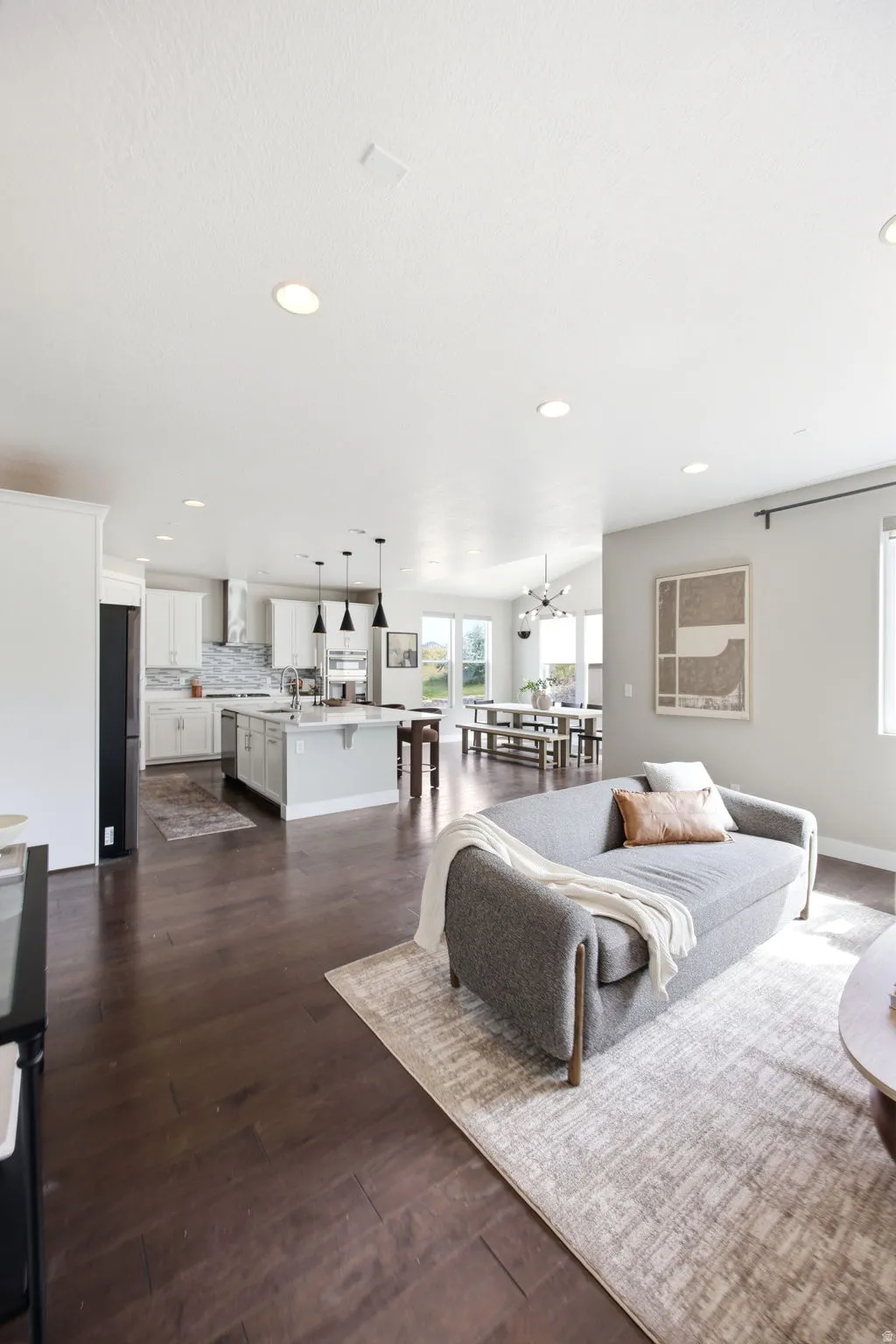 Spacious open-concept living area featuring dark wood-finish flooring, recessed lighting, and a modern kitchen with a large island