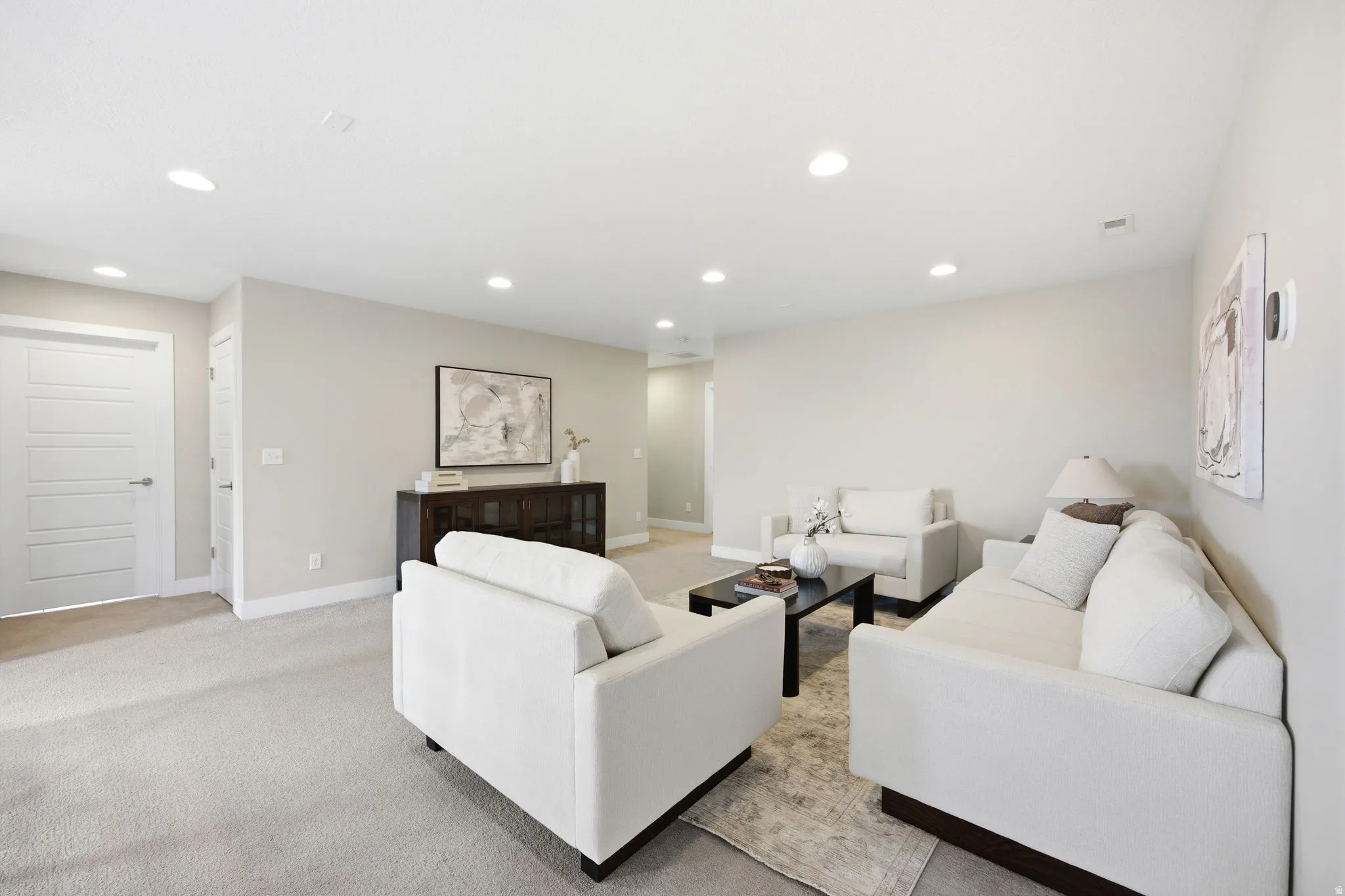 Spacious living area featuring neutral wall tones, recessed lighting, baseboard trim, and a contemporary five-panel interior door