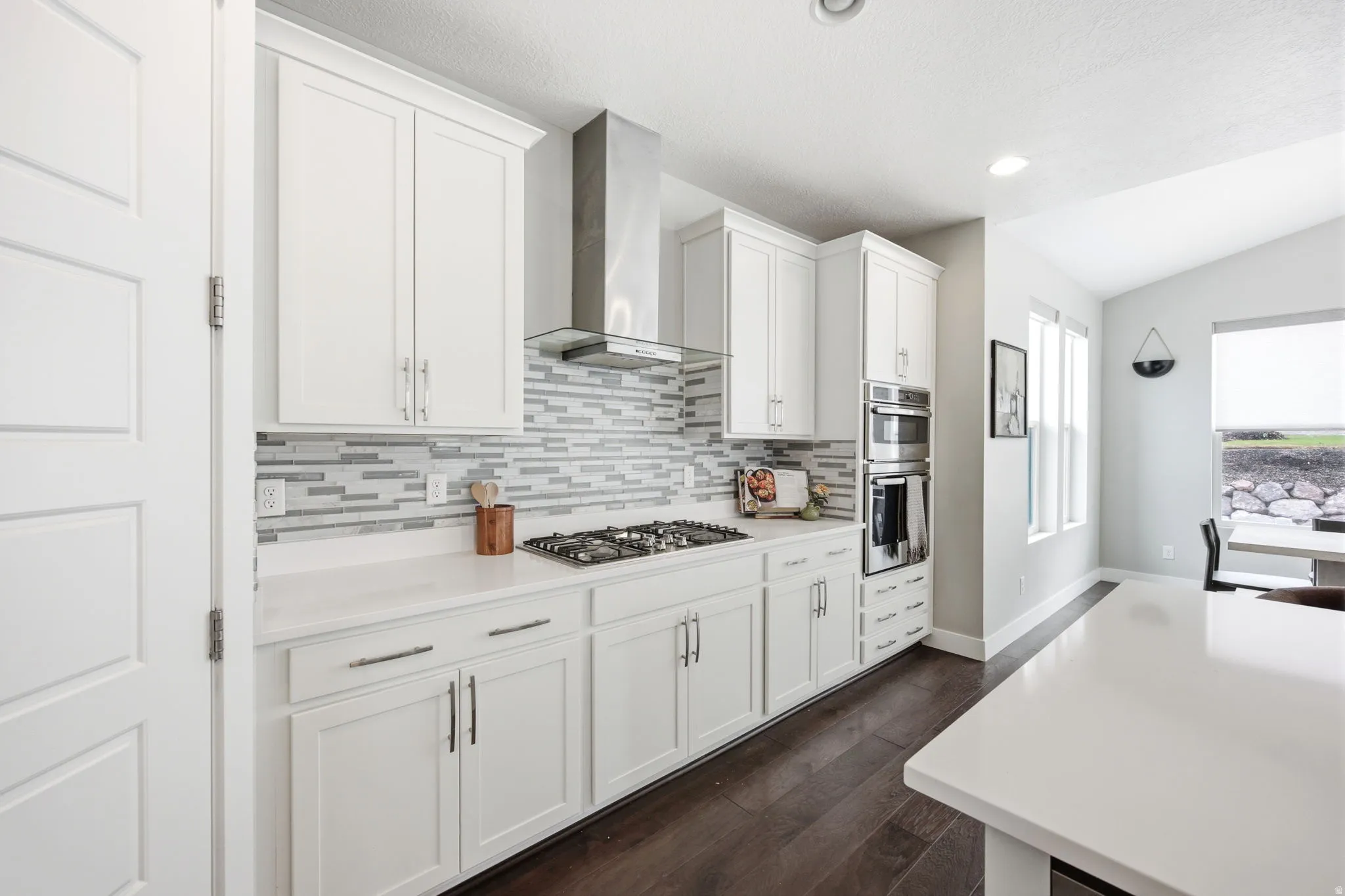 Contemporary kitchen featuring white cabinetry with silver hardware, a stainless steel range hood, and a built-in double oven