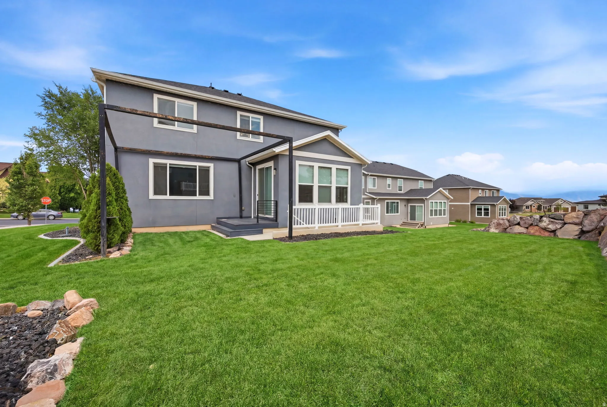 Expansive backyard featuring a large green lawn, rock landscaping, and a two-story residence with a patio and pergola structure