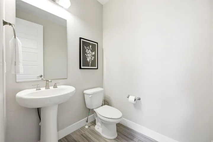 Pedestal sink with a brushed nickel faucet, large wall mirror, and wood-finish flooring