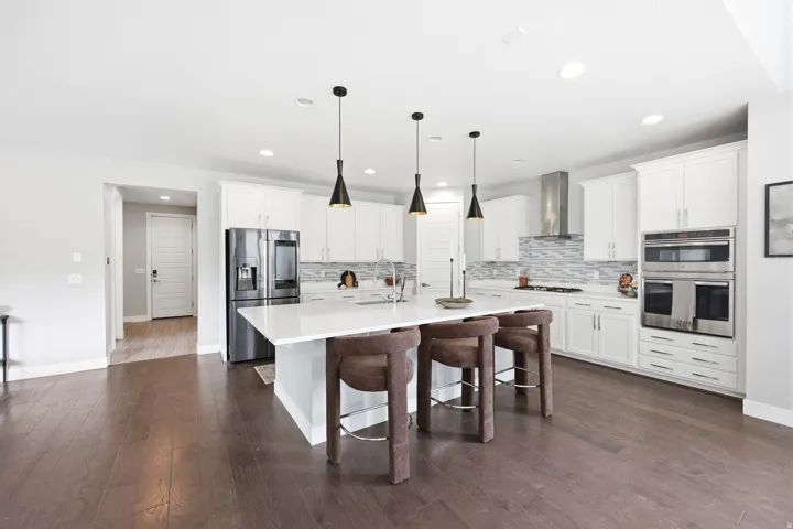 Expansive kitchen featuring a large island with seating, white shaker cabinetry, stainless steel appliances, and wood-finish flooring