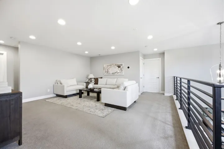 Versatile loft space featuring plush carpeting, recessed lighting, and a modern black horizontal railing