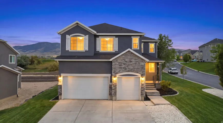 Two-story residence featuring a gray stucco exterior with stone accents, a two-car garage, and white window shutters