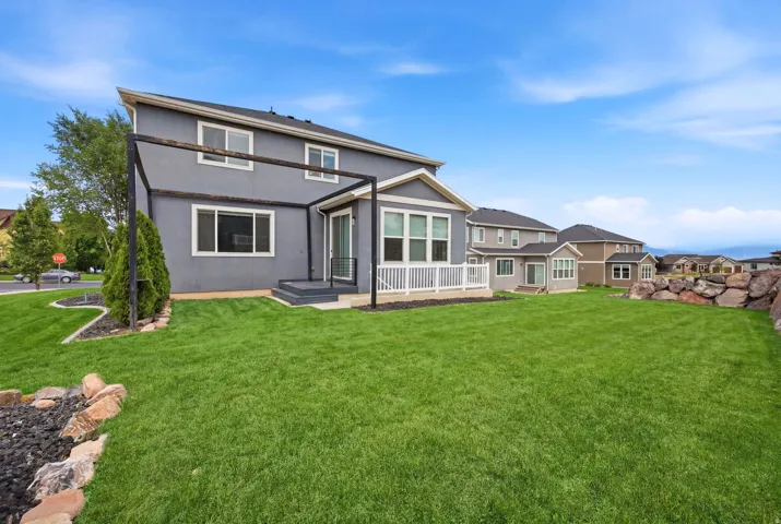 Expansive backyard featuring a large green lawn, rock landscaping, and a two-story residence with a patio and pergola structure