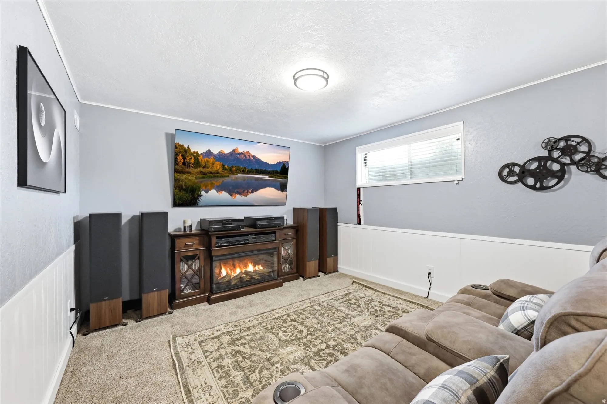 Entertainment room featuring a built-in electric fireplace with wood-finish cabinetry, a single window with horizontal blinds, and a neutral carpeted floor