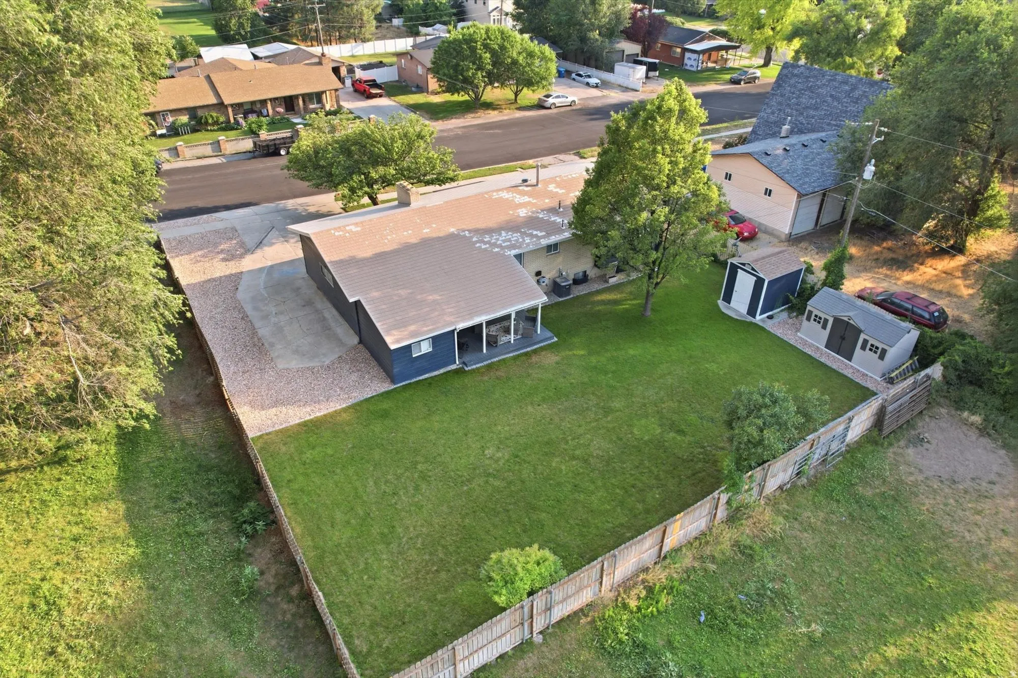 Expansive fenced yard featuring a manicured lawn, gravel driveway, and two storage sheds