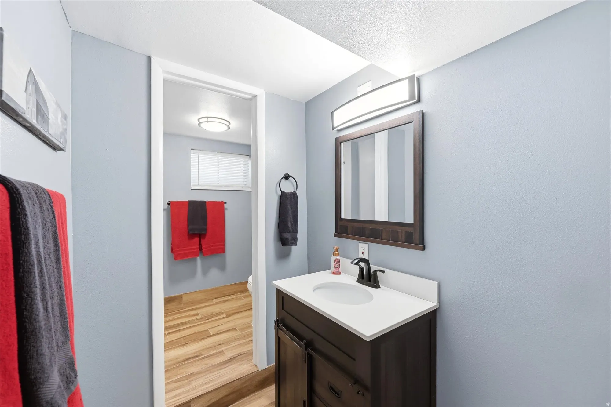 Vanity featuring a white countertop with an integrated sink, dark wood-finish cabinetry, and a dark-framed mirror