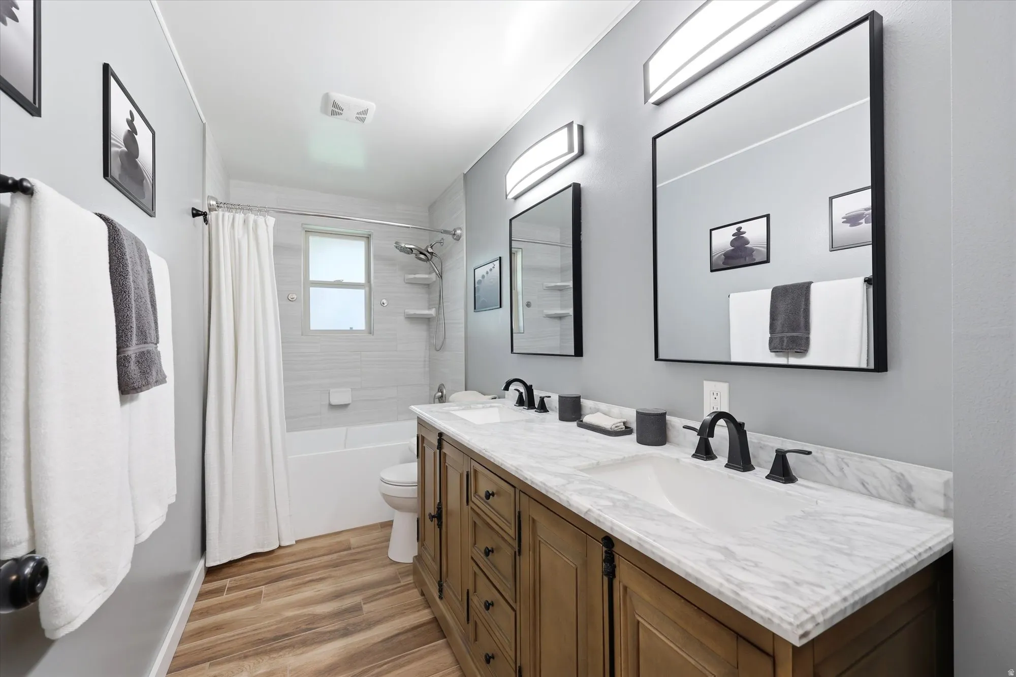 Bathroom featuring a dual vanity with a patterned countertop, wood-finish cabinetry, and matte black fixtures
