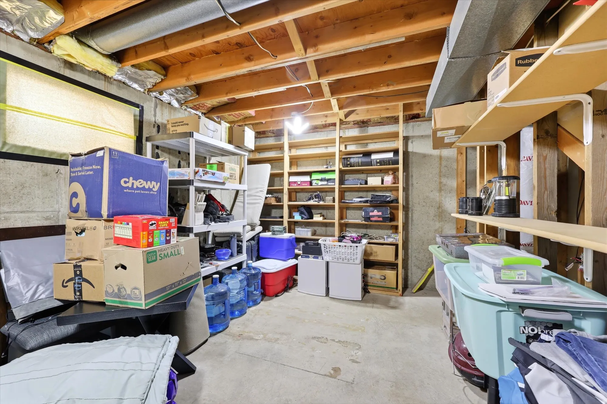Unfinished basement area featuring a concrete floor, exposed wood ceiling joists, and multiple built-in shelving units for storage