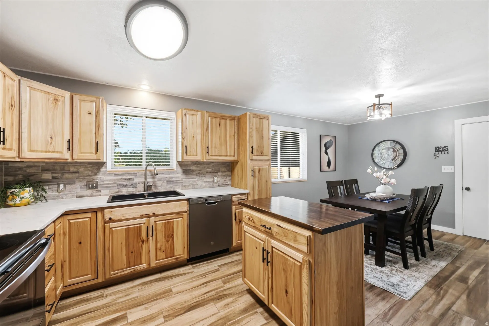 Kitchen and dining area featuring natural wood cabinetry, light countertops, stainless steel appliances, a center island with a wood-finish top, and wood-finish flooring
