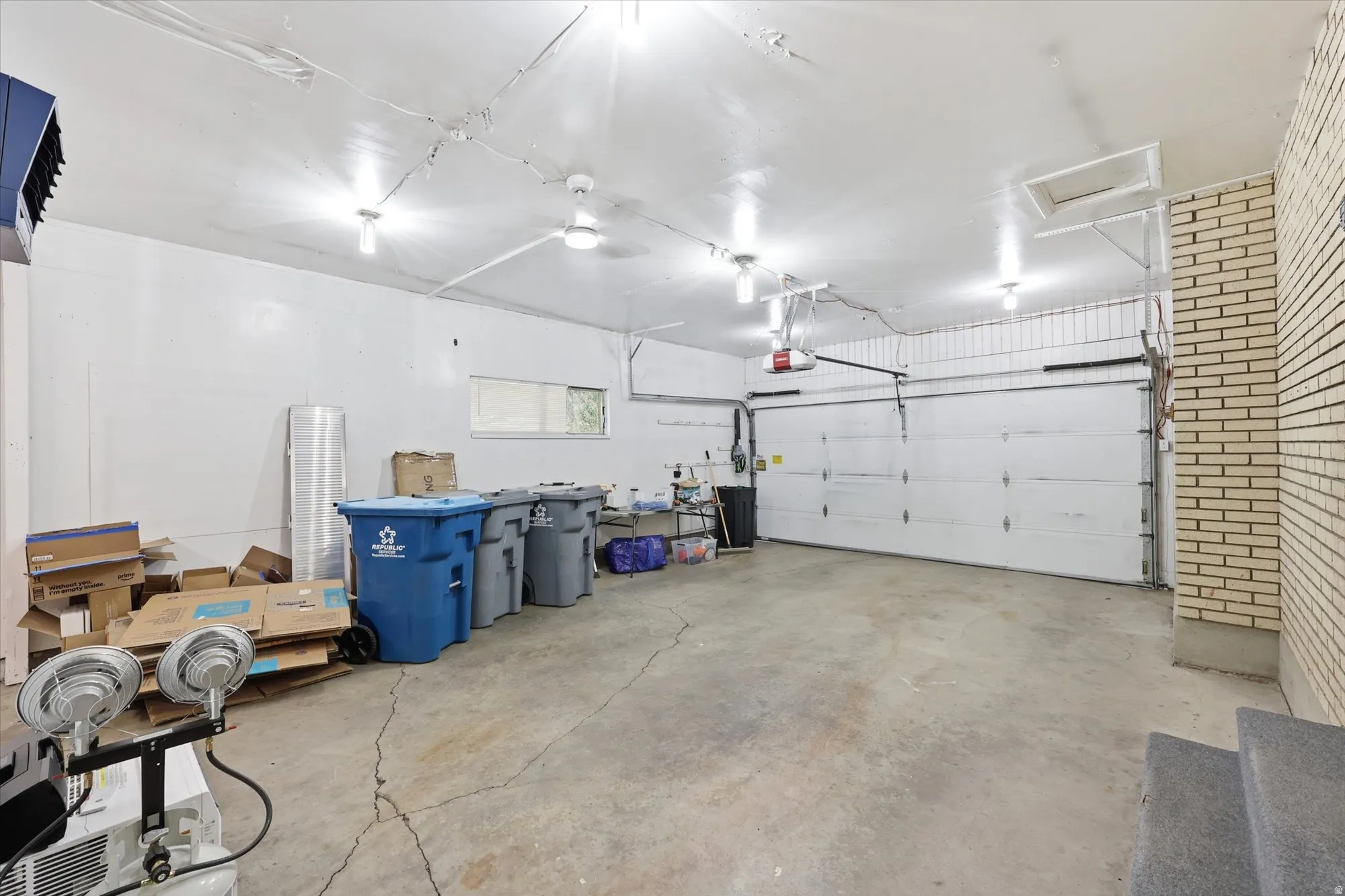 Spacious garage featuring a concrete floor, multiple ceiling-mounted light fixtures, a white overhead door, and a light-colored brick wall accent