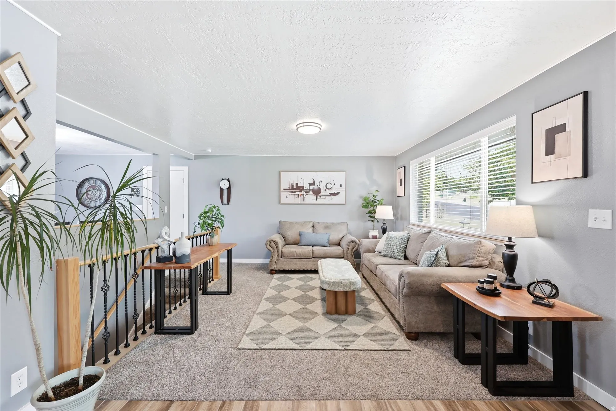 Spacious living area featuring light gray walls, carpet flooring, and a large window with blinds