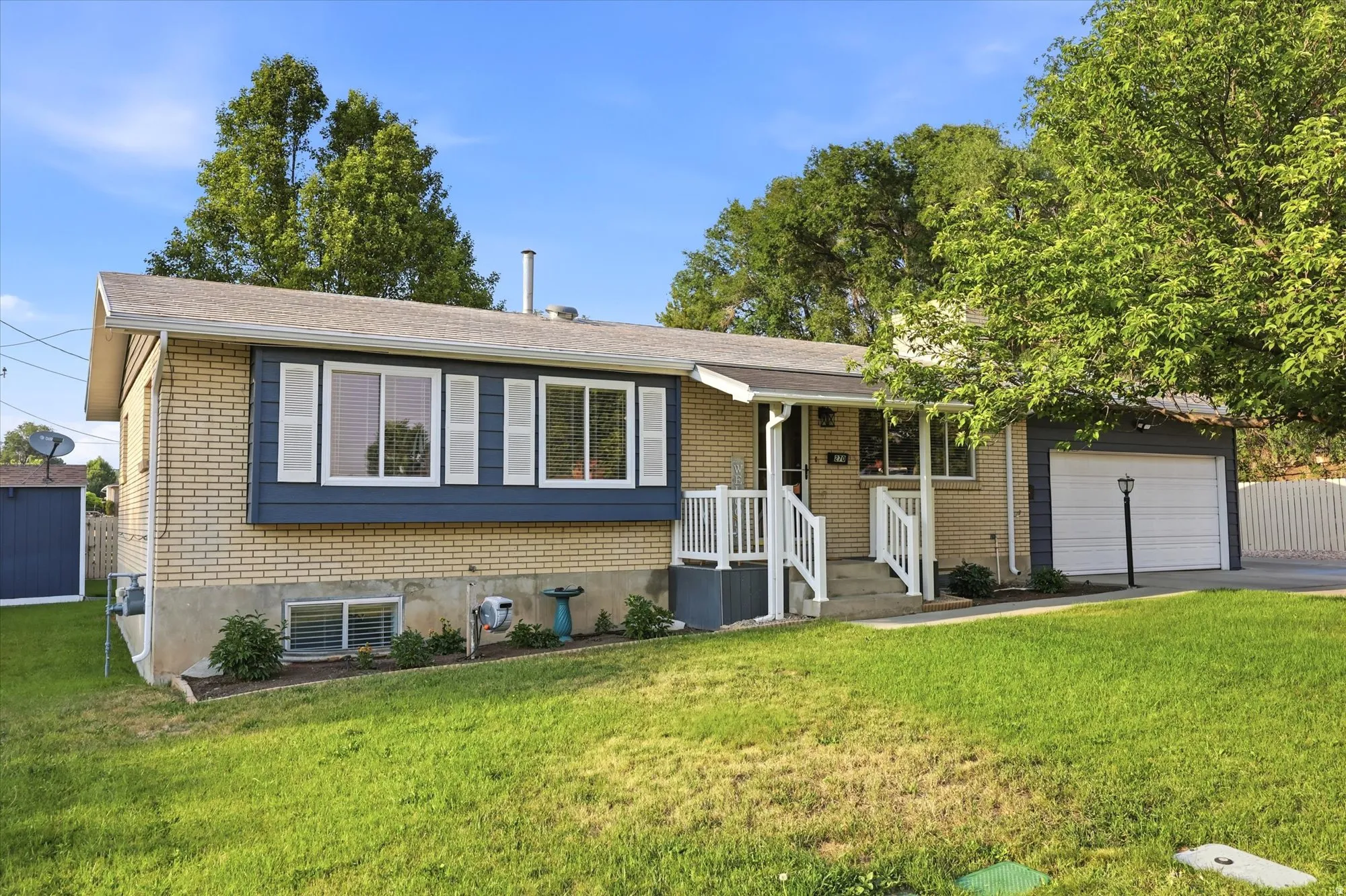 Exterior featuring light-colored brick siding, blue paneling, white window shutters, a white garage door, and a white-railed front porch