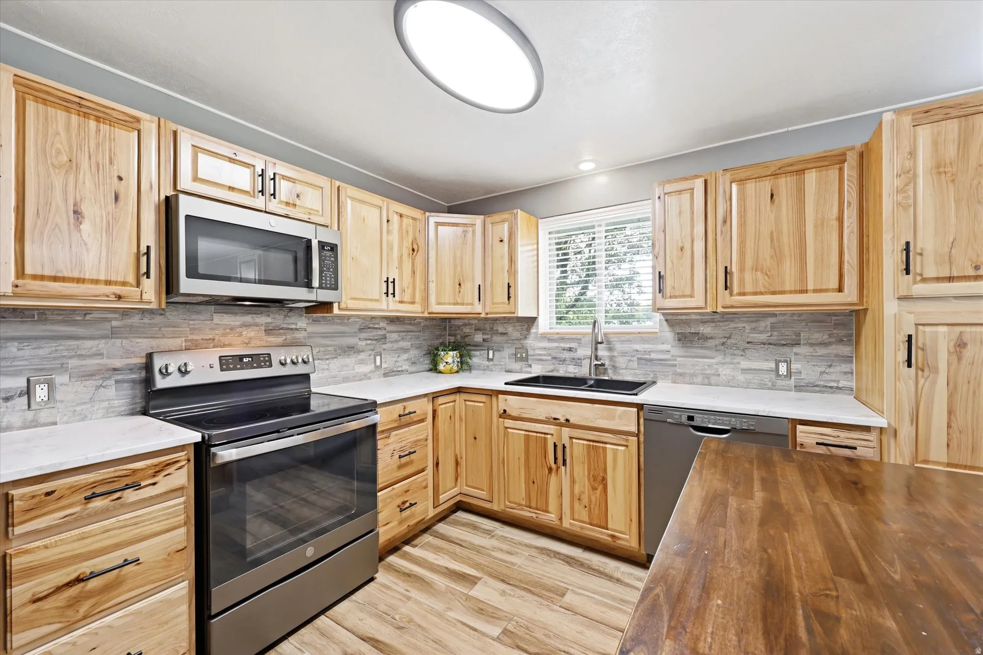 Bright kitchen featuring wood cabinetry, stainless steel appliances, a tile backsplash, light countertops, and wood-finish flooring