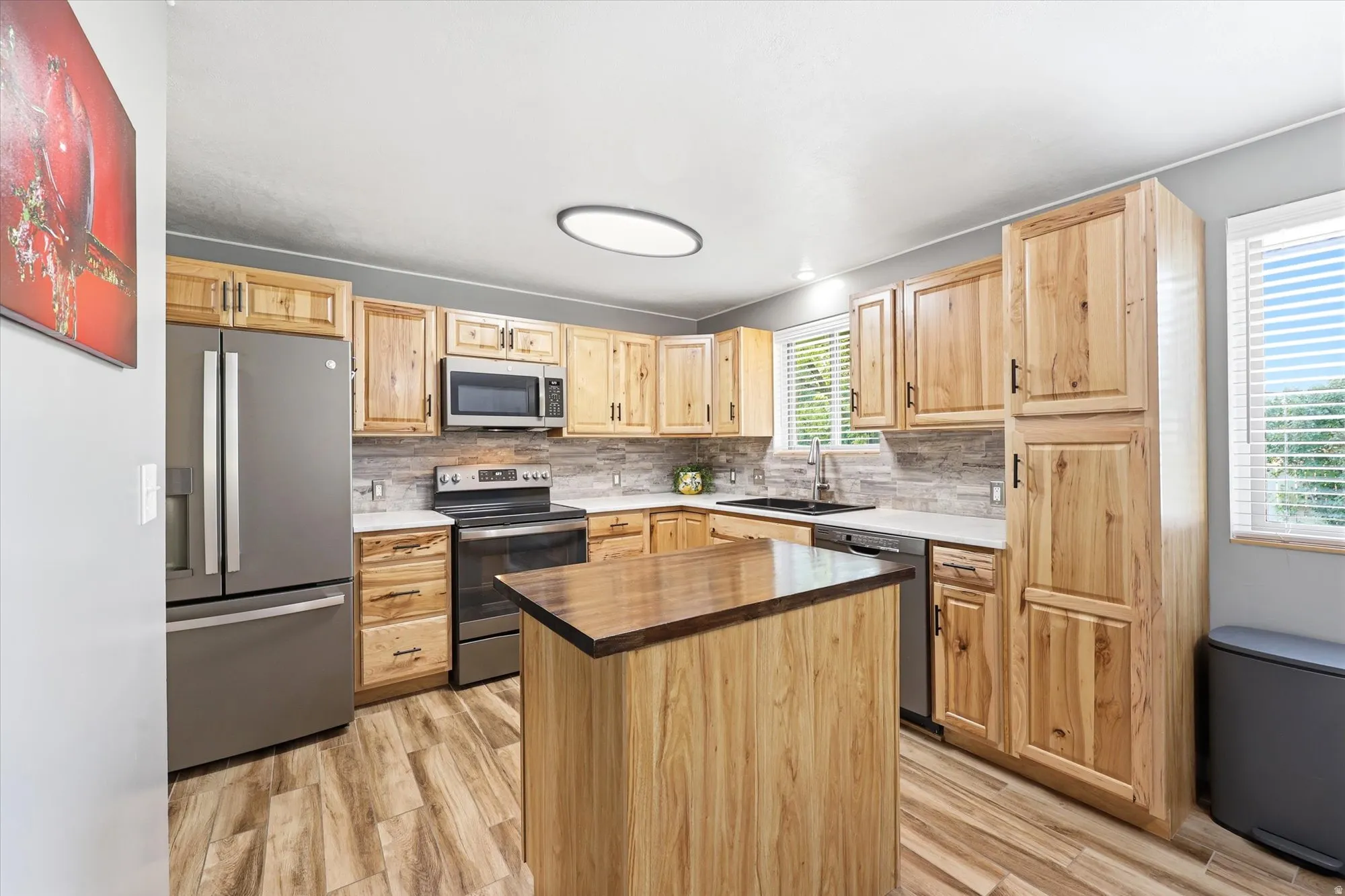 Well-appointed kitchen featuring light wood cabinetry, stainless steel appliances, a center island with a wood-finish countertop, white countertops, and wood-finish flooring