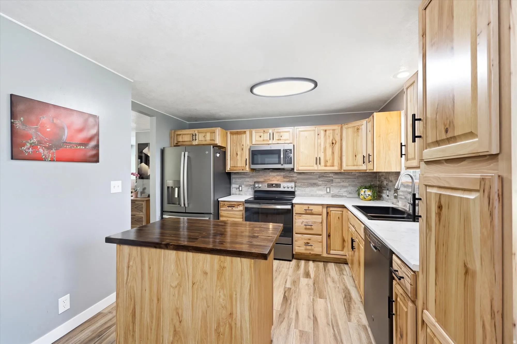 Kitchen featuring wood-finish cabinetry, stainless steel appliances, a white countertop, and a wood-finish island with a dark countertop