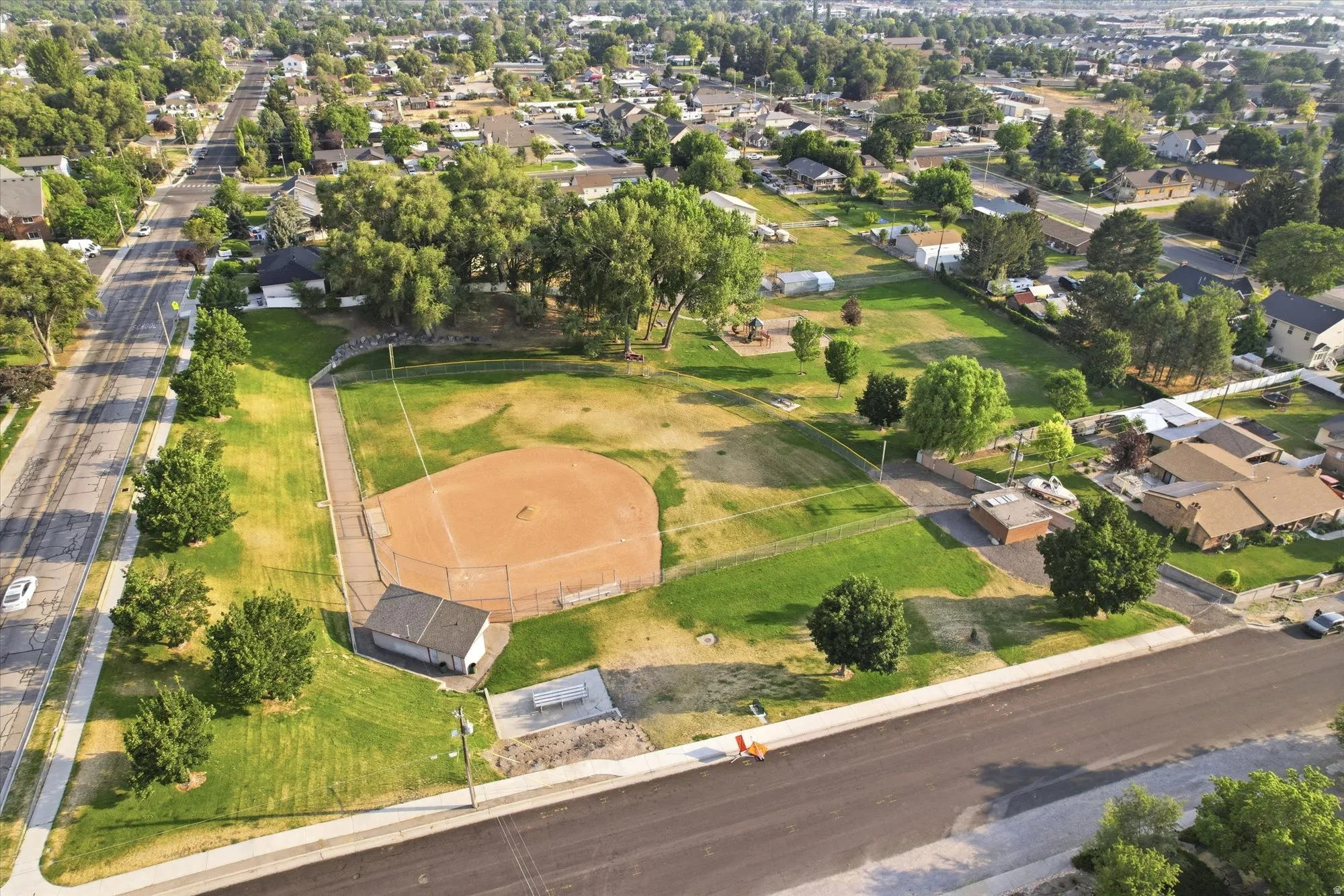 Neighborhood aerial featuring a baseball field with a dugout, open green spaces, and mature trees